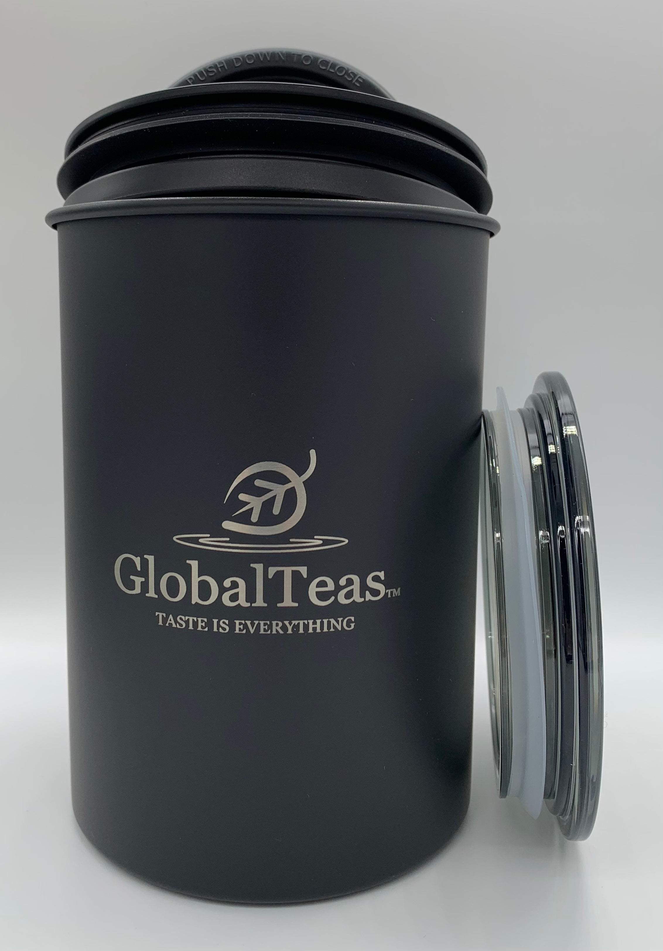 Matte black GlobalTeas canister with "Taste is Everything" slogan and extra lids beside it.