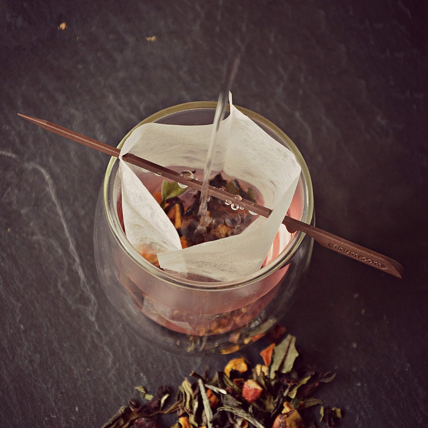 A glass filled with tea, featuring a tea bag and a tea filter stick for brewing convenience.